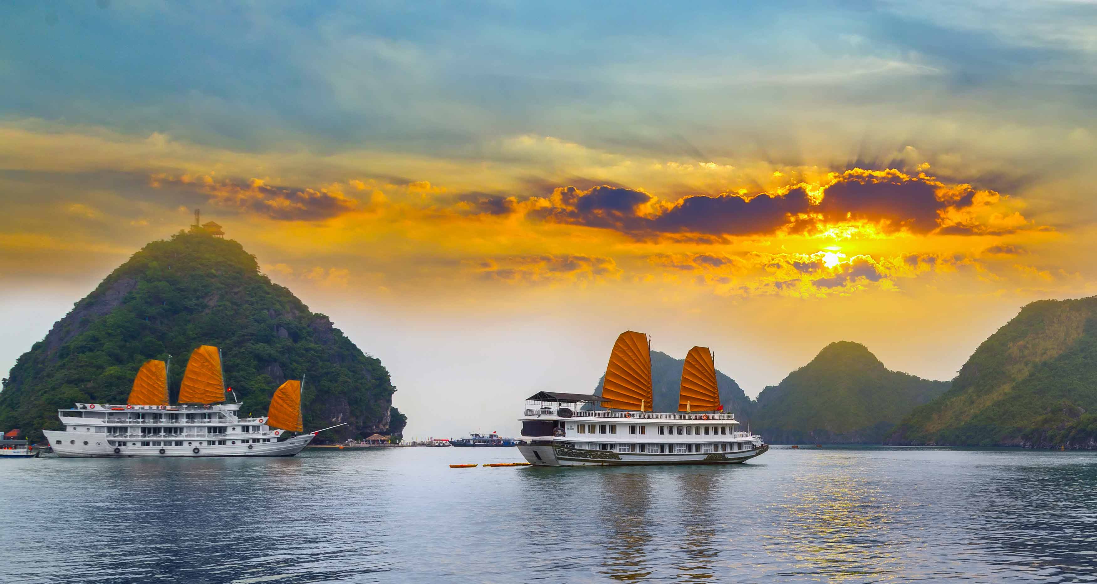 A traditional junk boat sailing through the calm water of Halong Bay, with limestone cliffs in the background.